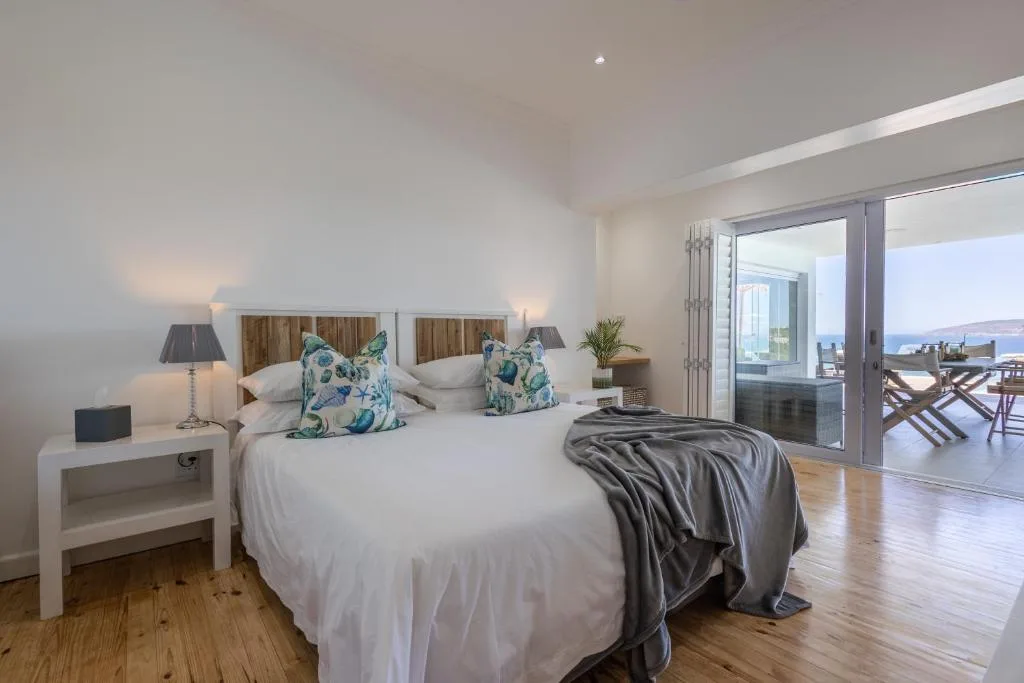 Bright bedroom with queen bed, coastal views through glass doors to deck
