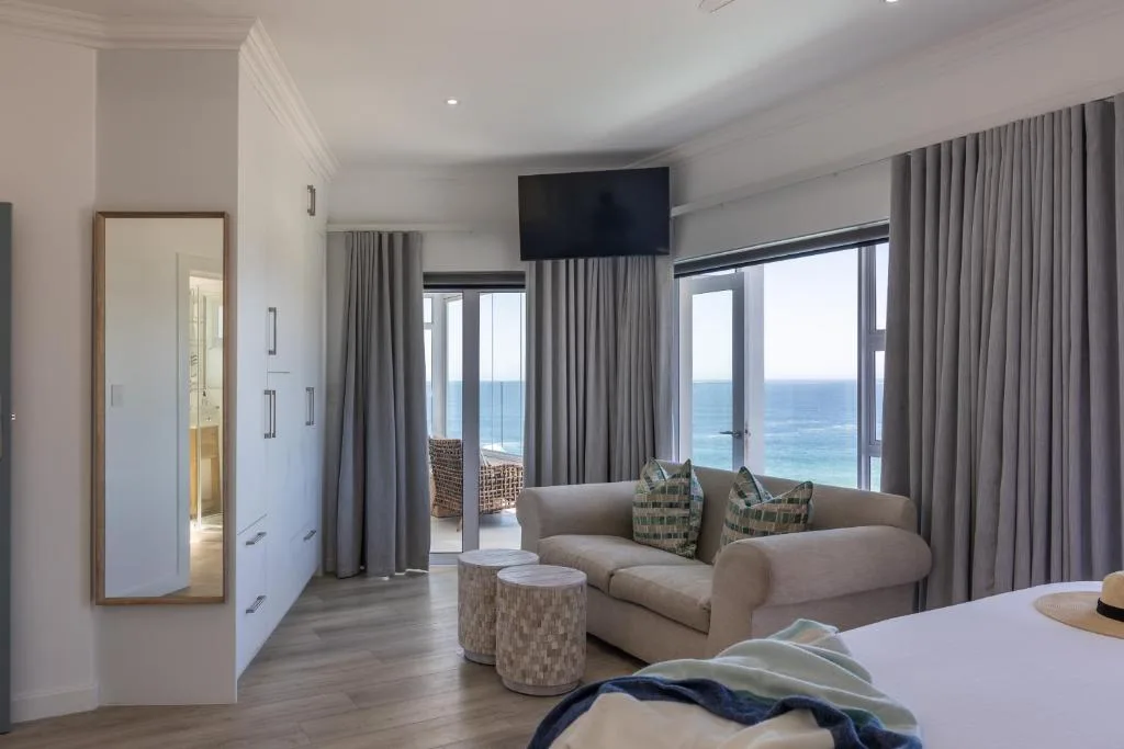 Spacious bedroom with ocean view through floor-to-ceiling windows and lounge area