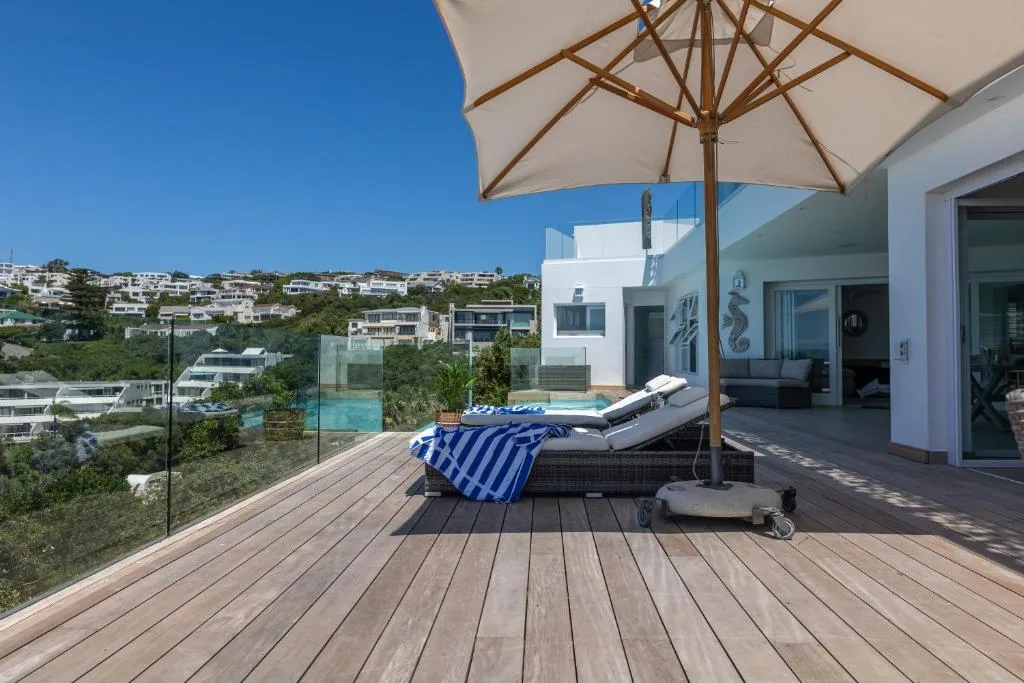 Wooden deck with lounger, umbrella, and pool view overlooking hillside homes