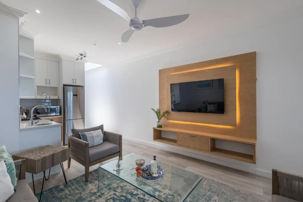 Modern lounge with wall-mounted TV, comfortable seating, and open-plan kitchen