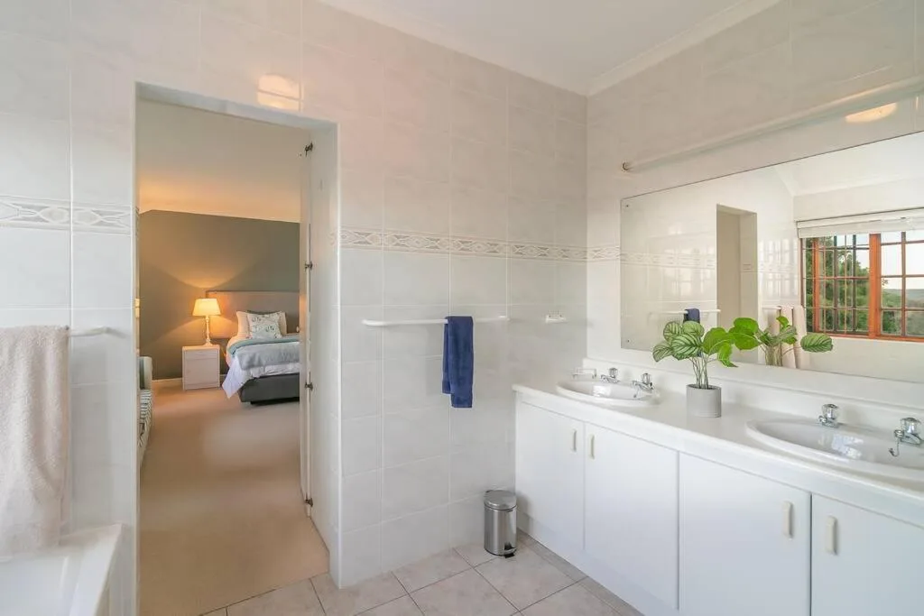 Bright bathroom with dual vanities, large mirror, and tiled shower area