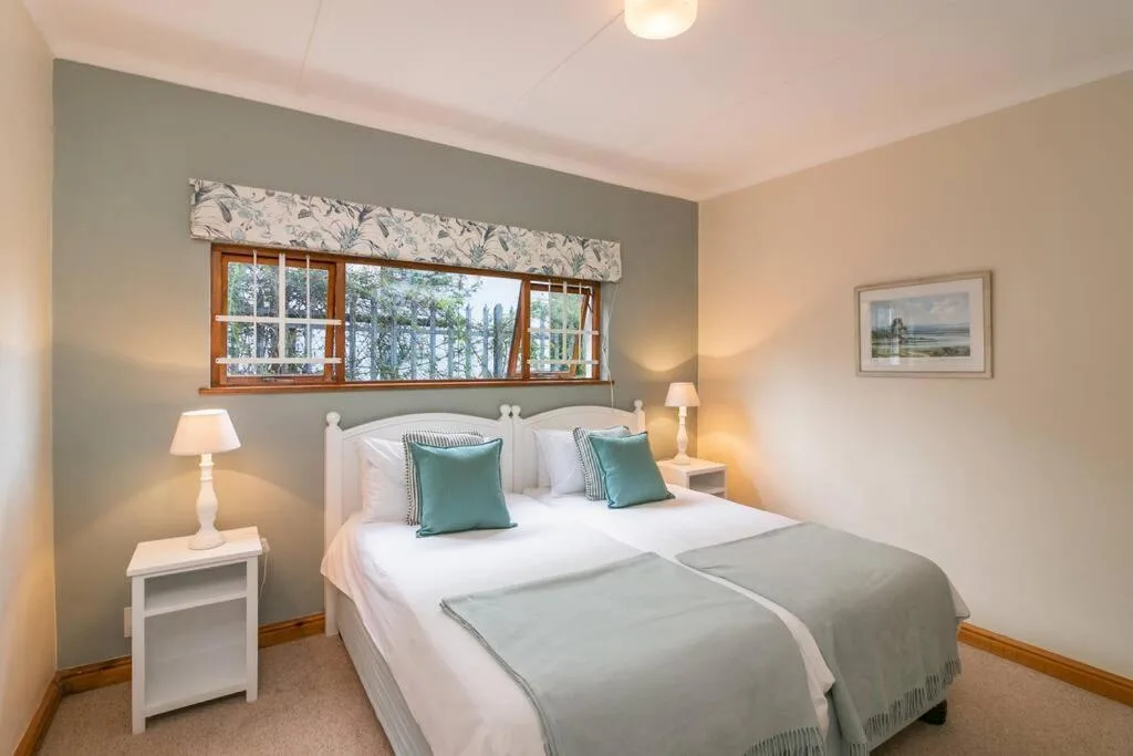 Bright bedroom with double bed, teal cushions, bedside lamps, and window view