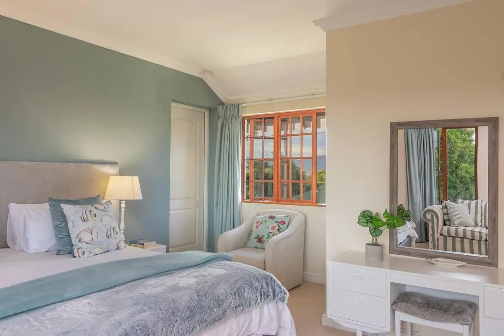 Spacious bedroom with sage green accent wall, comfortable bed, and garden views