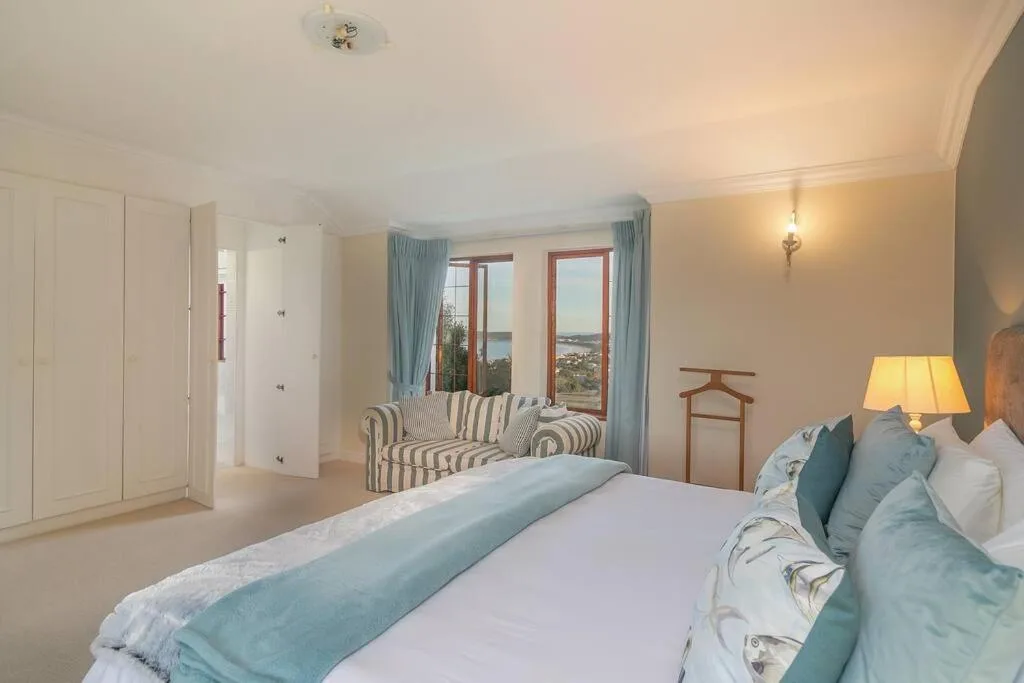 Spacious bedroom with bed, striped armchair, and scenic coastal views through windows
