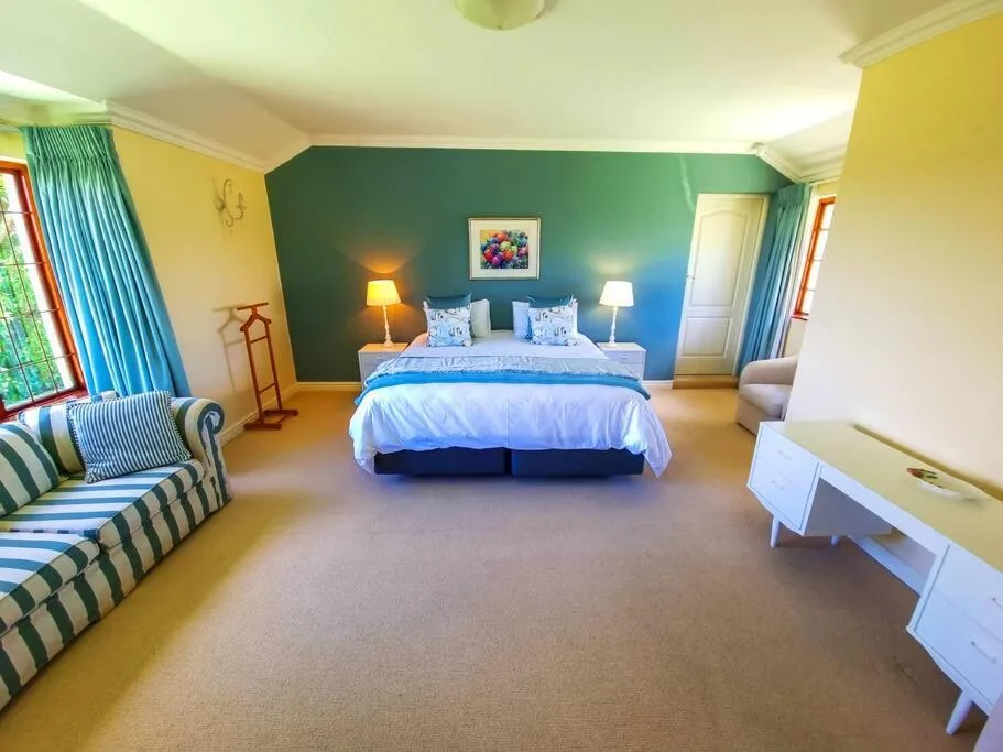 Spacious bedroom with queen bed, green accent wall, and striped armchair