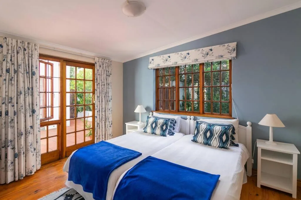 Bright bedroom with twin beds, blue throws, and wooden French doors opening onto a terrace
