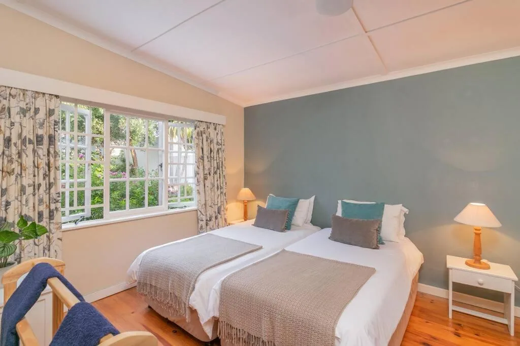 Bright bedroom with twin beds, blue accent wall, garden views through large windows