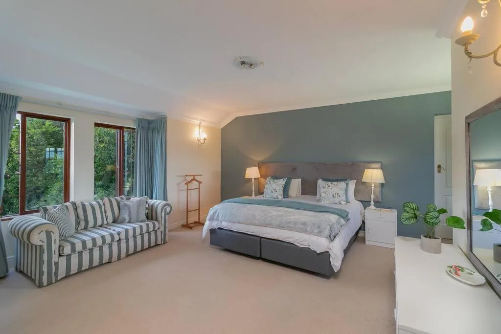 Spacious master bedroom with king bed, striped sofa, garden views, and ensuite bathroom