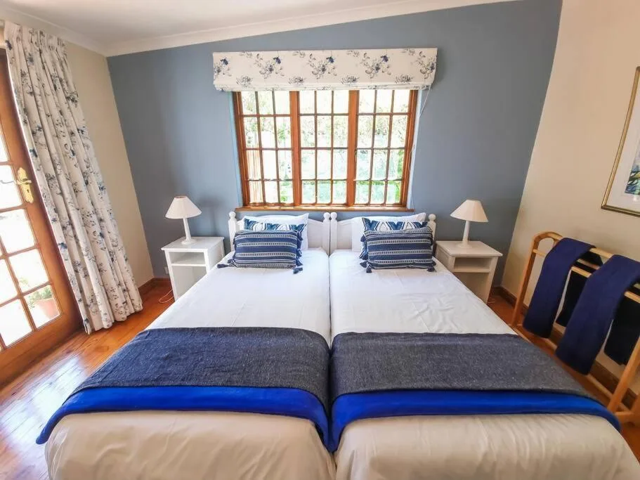 Bright bedroom with twin beds, blue accents, wooden floors, and garden views