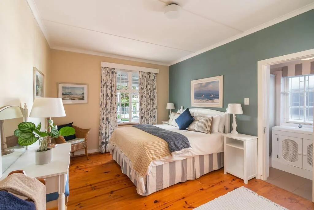 Bright bedroom with queen bed, sage green accent wall, wooden floors