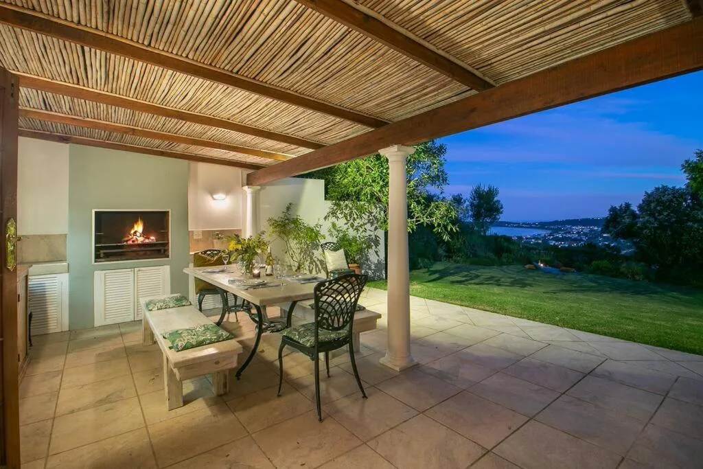 Covered patio with dining table, fireplace, and lagoon views at dusk