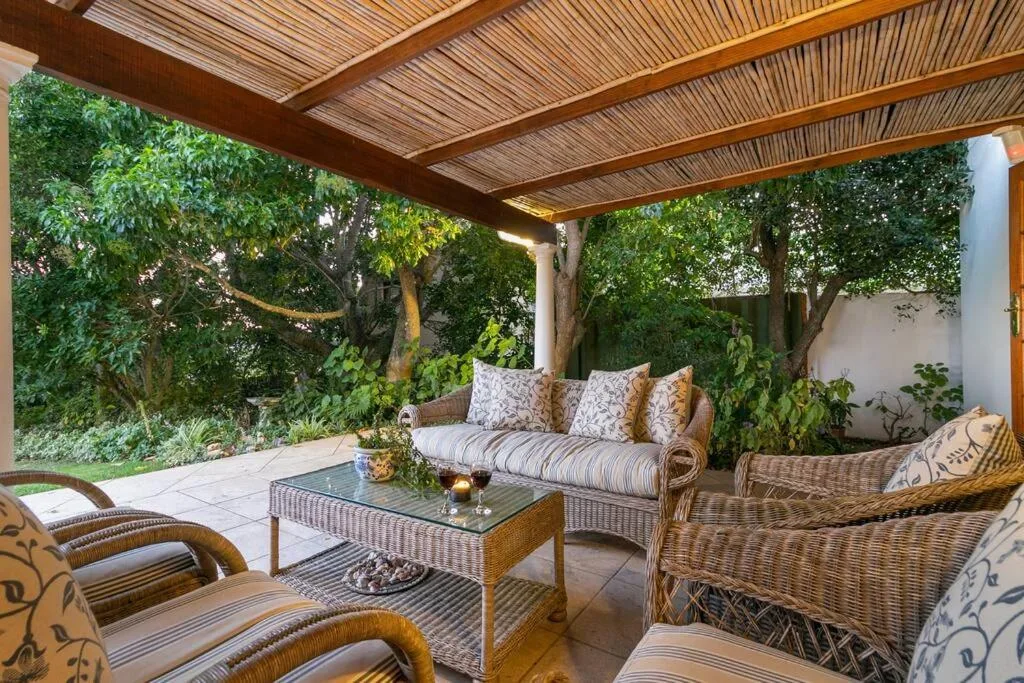 Covered patio with wicker furniture overlooking lush garden vegetation