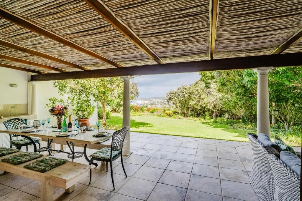 Covered patio with dining table overlooking manicured garden and distant hills