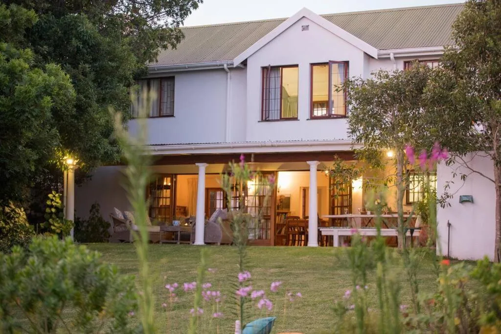 White holiday home with illuminated porch and manicured garden at dusk