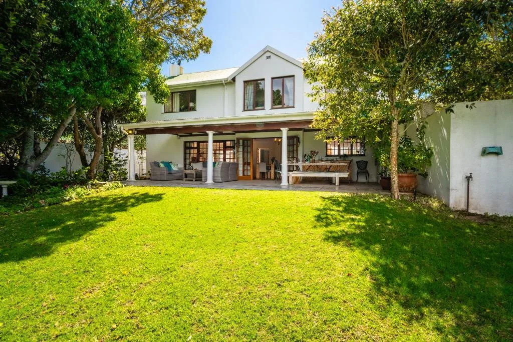 White two-story house with wraparound porch and lush green lawn