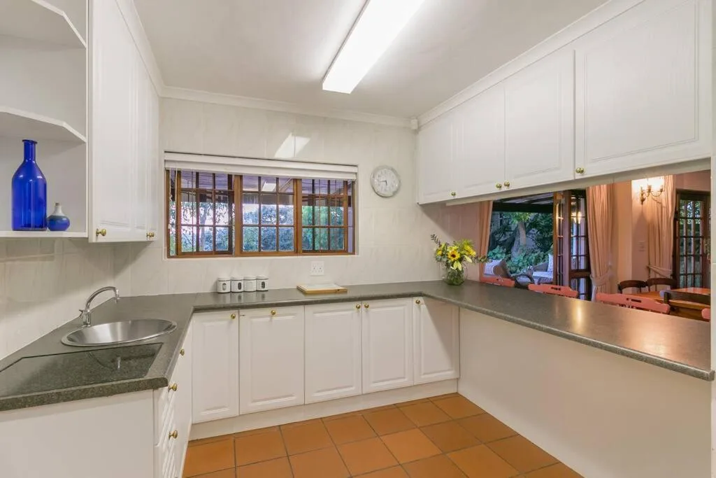 Bright white kitchen with granite counters and wooden-framed windows overlooking garden