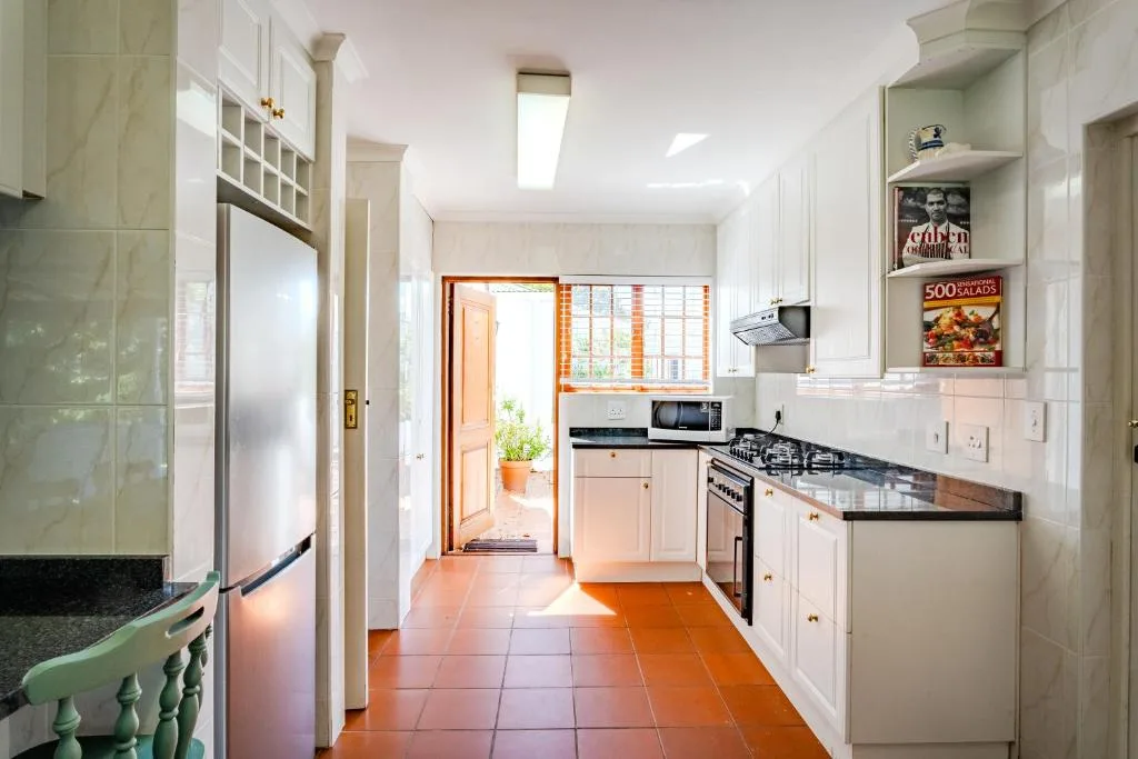 Bright galley kitchen with white cabinetry, gas stove, and terracotta tile flooring
