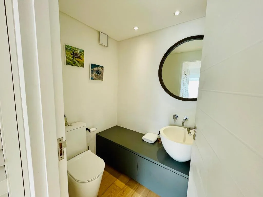 Modern bathroom with round mirror, white vessel sink, and toilet