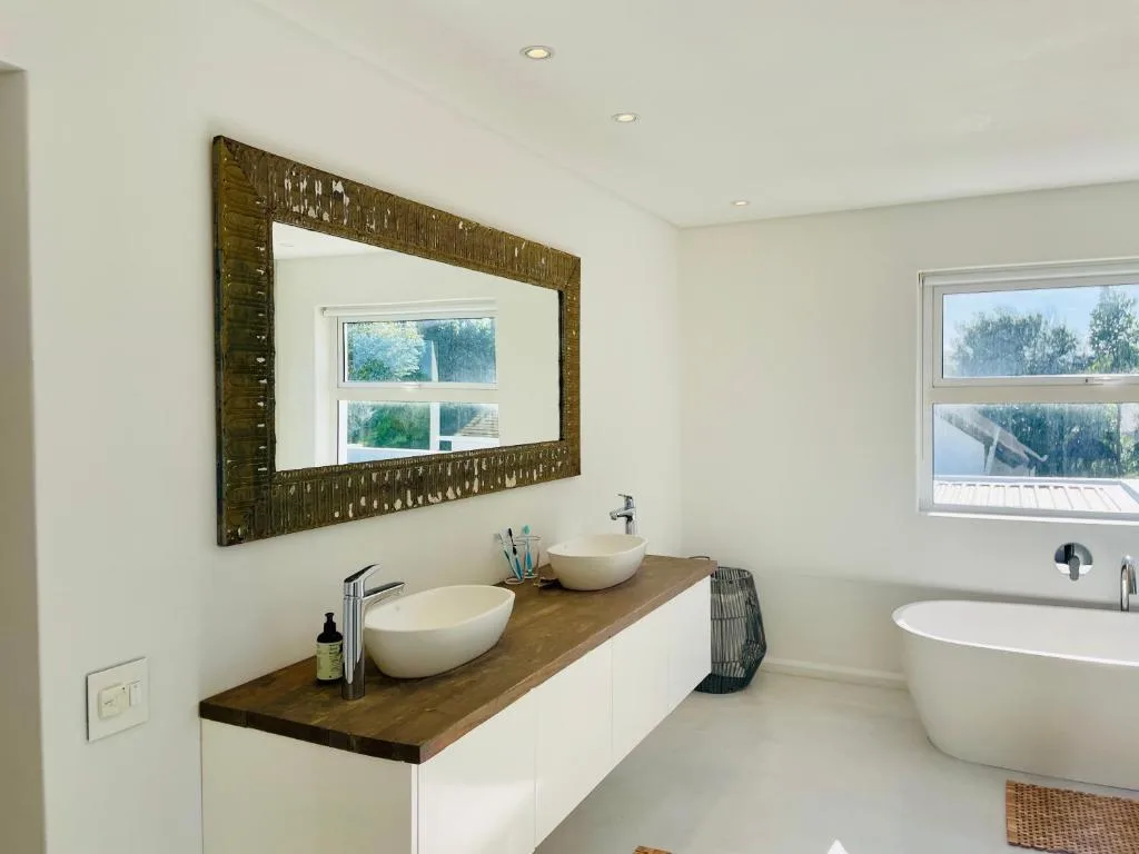 Modern bathroom with dual vanity sinks, decorative mirror, and freestanding tub