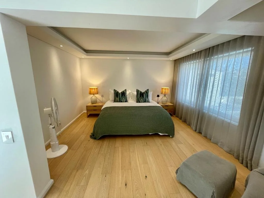 Spacious bedroom with king bed, wooden floors, and sheer curtains