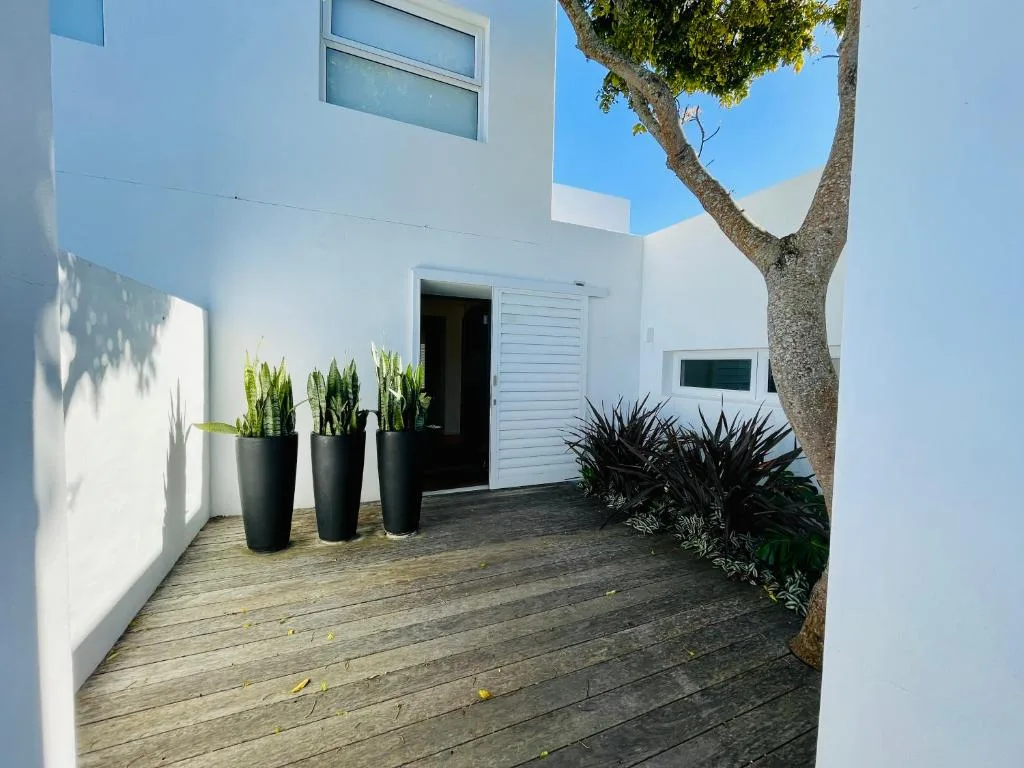 Modern white villa entrance with wooden deck and potted plants