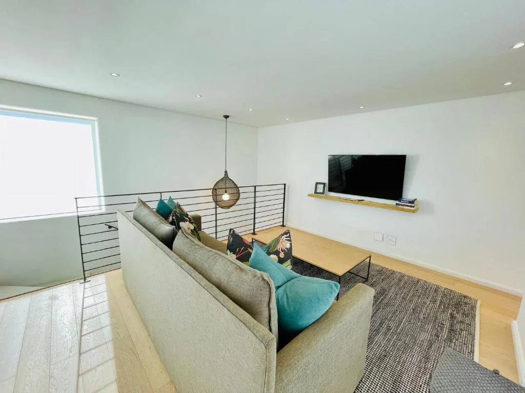 Modern living room with gray sofa, turquoise cushions, mounted TV, and wooden flooring