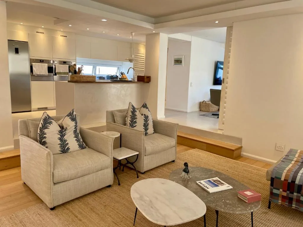 Modern lounge with cream armchairs, marble table, and open-plan kitchen view