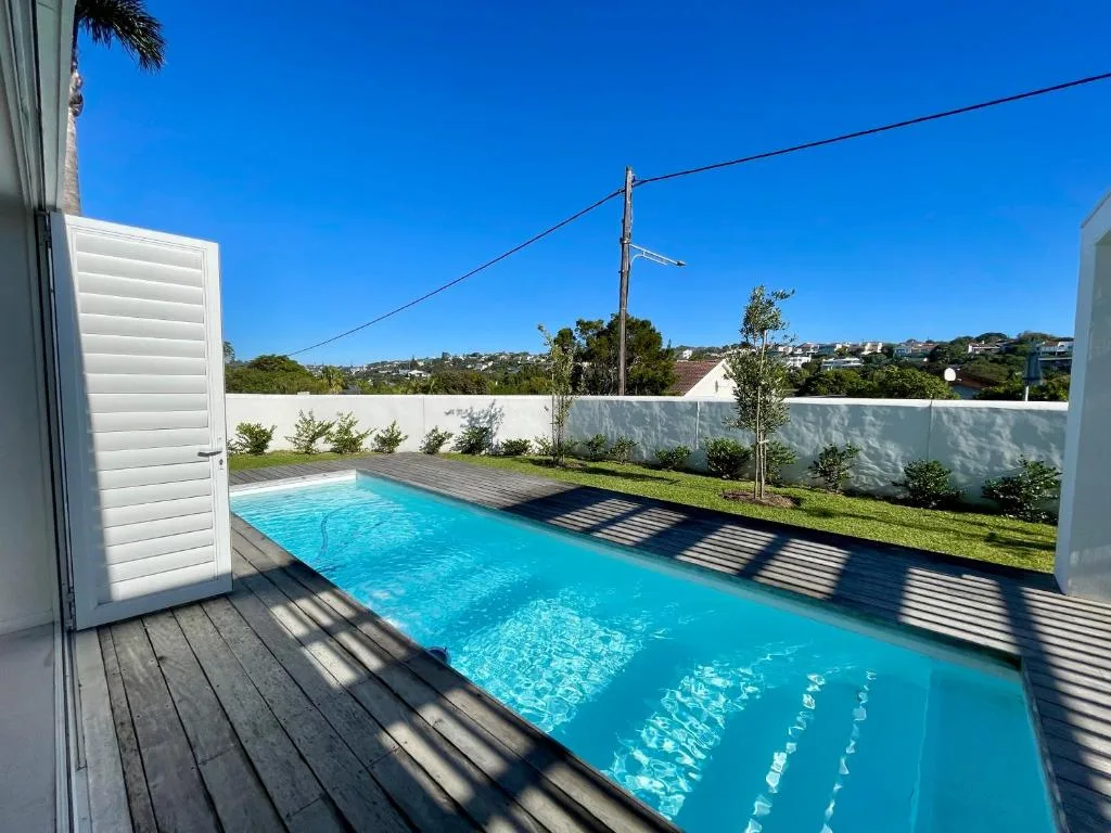 Rectangular swimming pool with clear turquoise water, wooden deck, white boundary wall