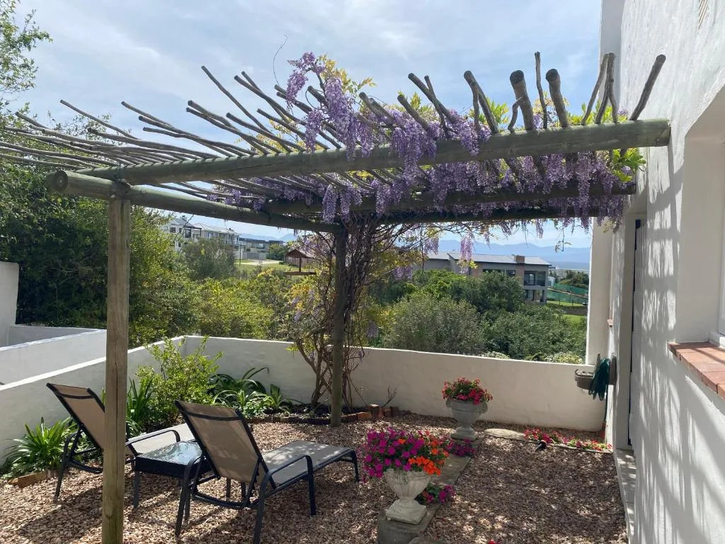 Shaded patio with wisteria pergola, loungers, and flowering plants overlooking gardens