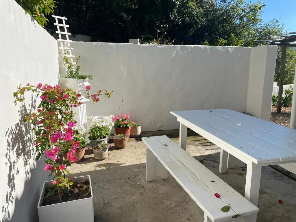 White outdoor dining area with benches and potted flowers blooming bright pink