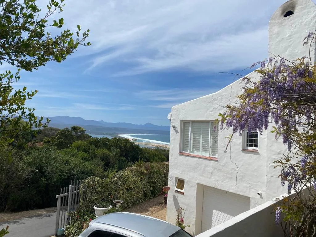 White coastal cottage with purple wisteria, mountains and beach view beyond