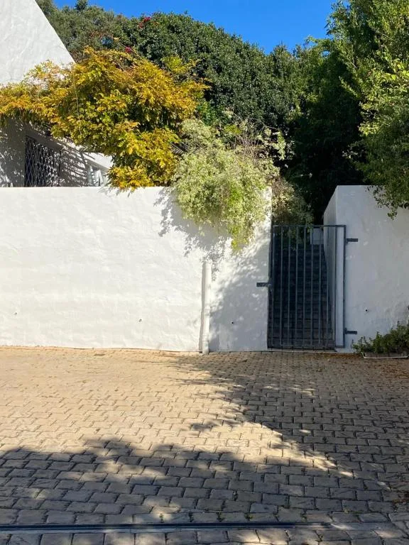 White-walled cottage entrance with black gate and lush garden trees