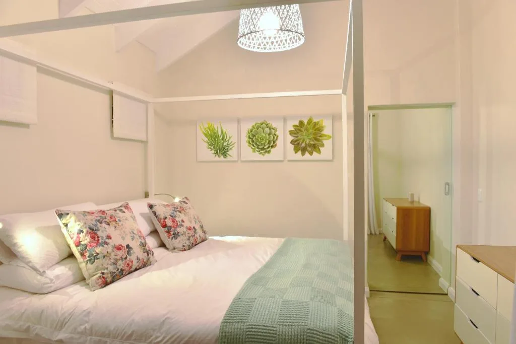 Bright bedroom with double bed, floral pillows, and succulent wall art