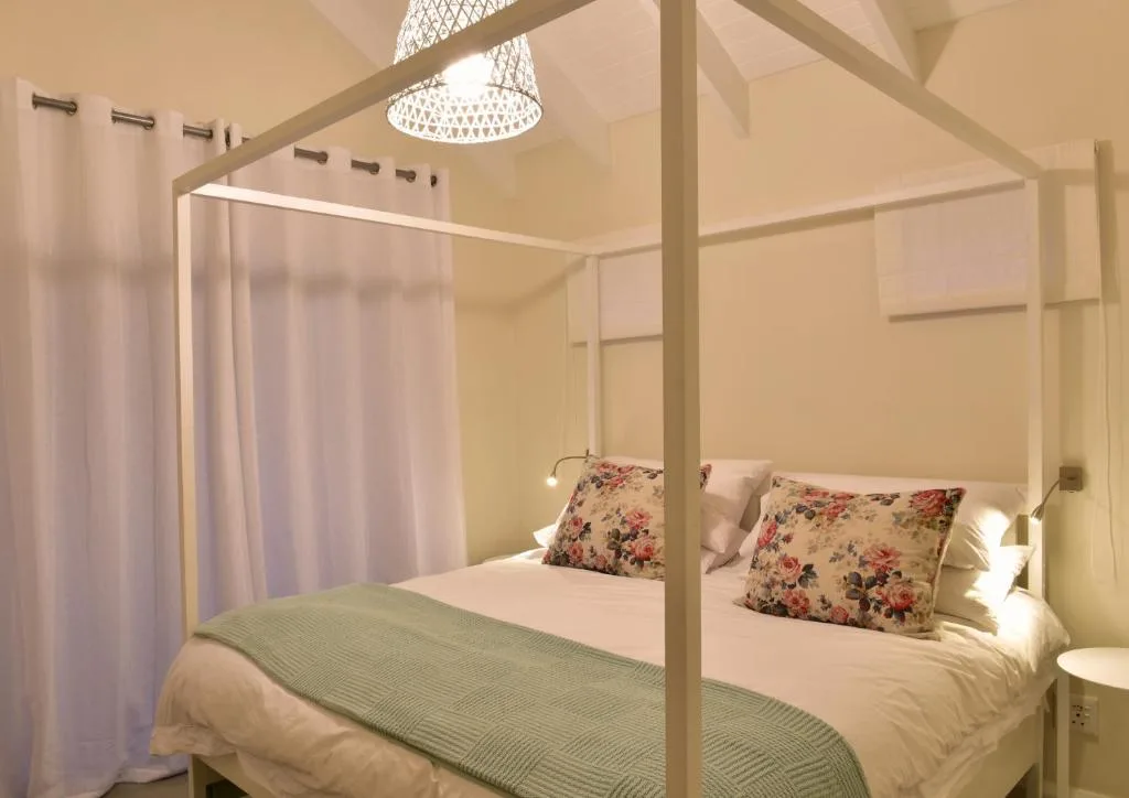 Four-poster bed with floral pillows and green bedspread in bright room