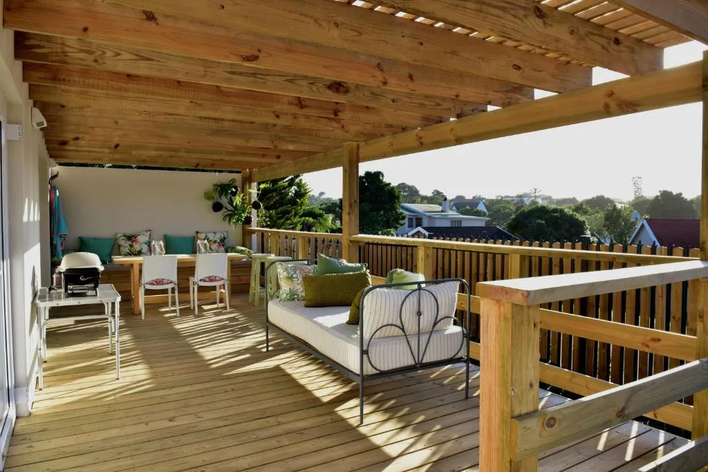 Wooden deck with covered pergola, seating, and garden view