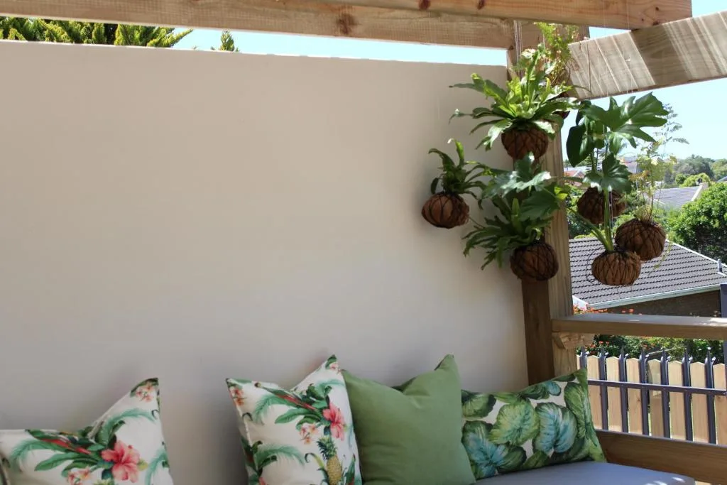 Covered outdoor deck with comfortable seating and hanging plants, overlooking gardens