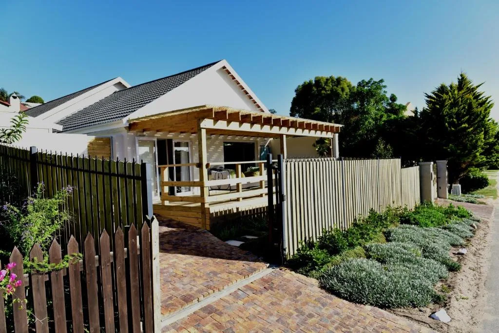 Modern white cottage with wooden pergola deck and manicured gardens, fenced entrance