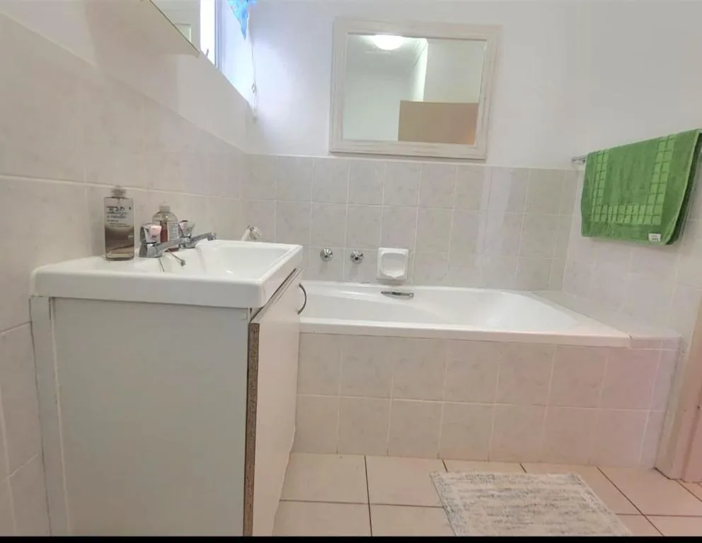 Clean bathroom with white vanity sink, bathtub, and green towel