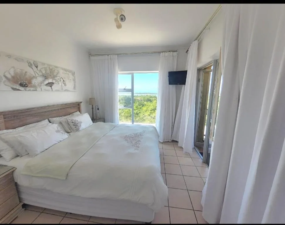 Bright bedroom with queen bed, white linens, and scenic lagoon view through glass doors