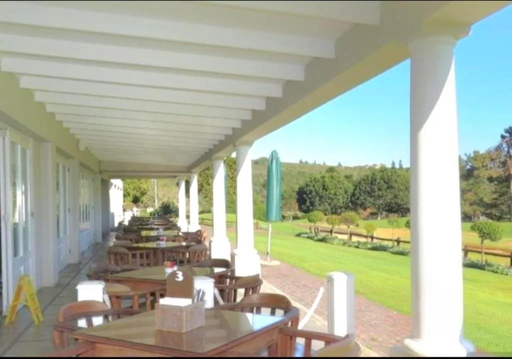 Covered veranda with dining tables overlooking lush garden and green hills