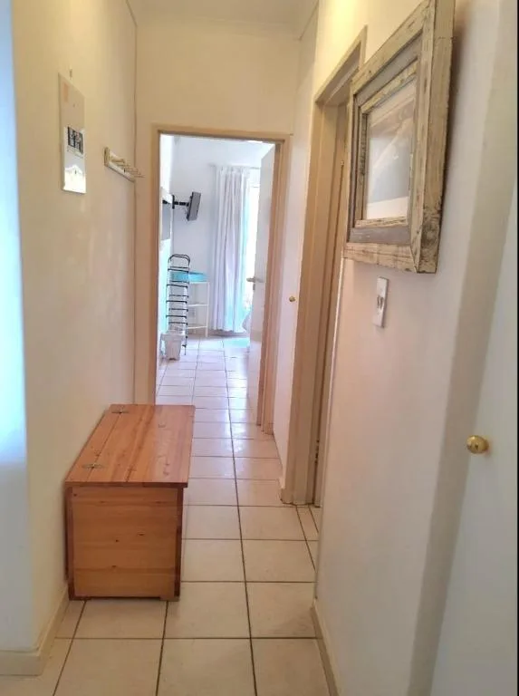 Narrow hallway with wooden chest and tiled flooring, leading to rooms