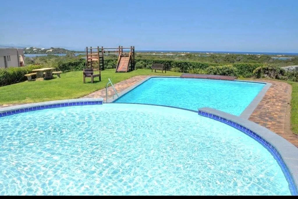 Two swimming pools with brick patio and sea views beyond green lawn