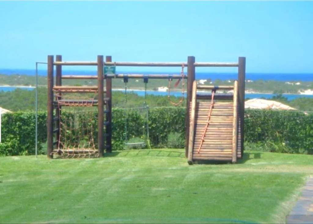 Coastal vista with playground structure overlooking blue lagoon and forested landscape