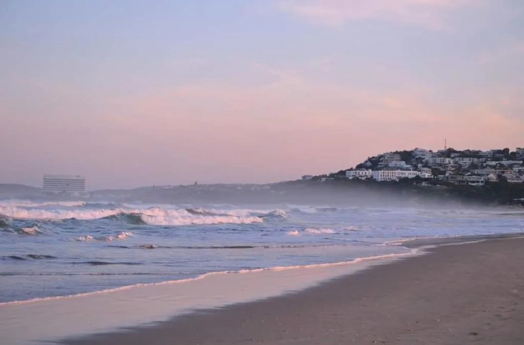 Sunrise over Plettenberg Bay beach with rolling waves and coastal town