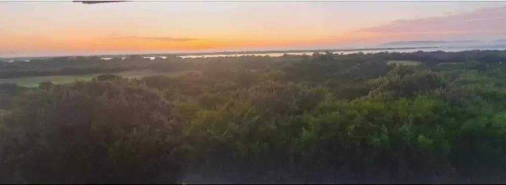 Sunset over forested valleys and distant lagoon waters from elevated vantage point