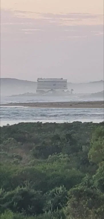 Coastal landscape with lagoon, vegetation, and distant buildings at dusk