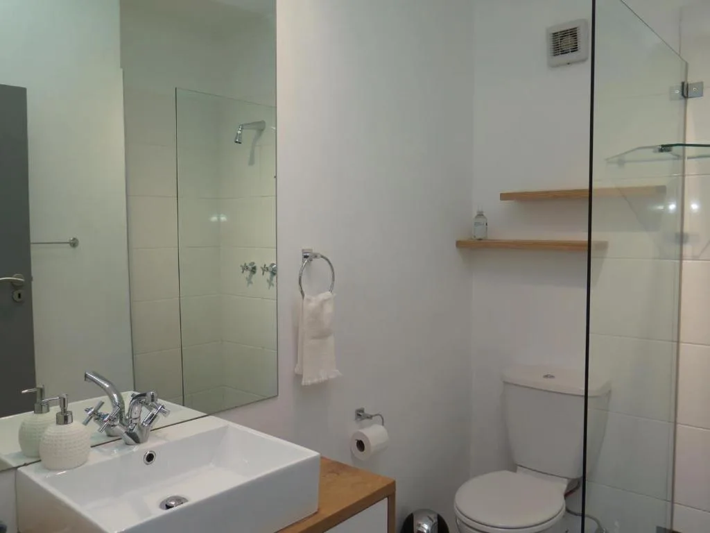 Modern bathroom with white sink, glass shower enclosure, and wooden shelving