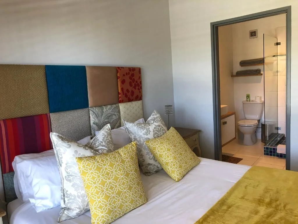 Bright bedroom with colorful patchwork headboard and ensuite bathroom visible