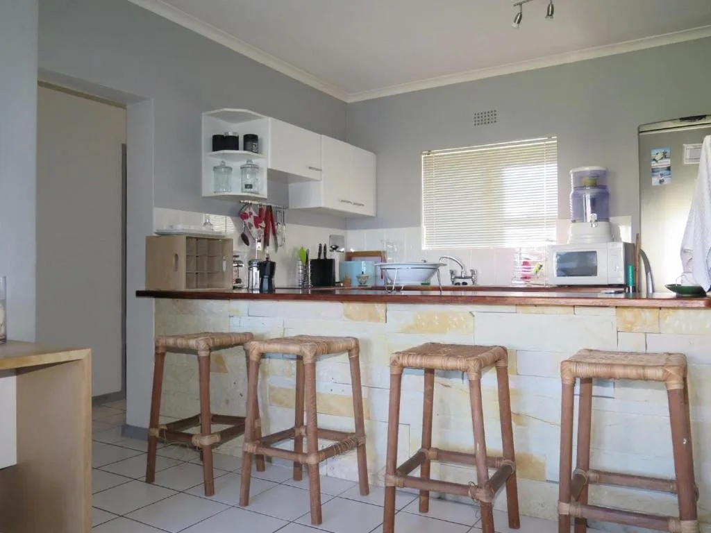 Modern kitchen with white cabinetry, wood countertop, and four woven bar stools