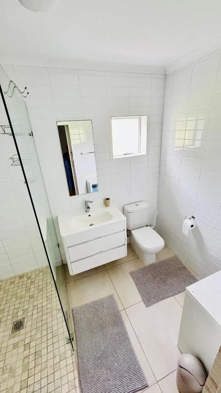 Clean modern bathroom with white vanity, mirror, toilet, and glass shower enclosure